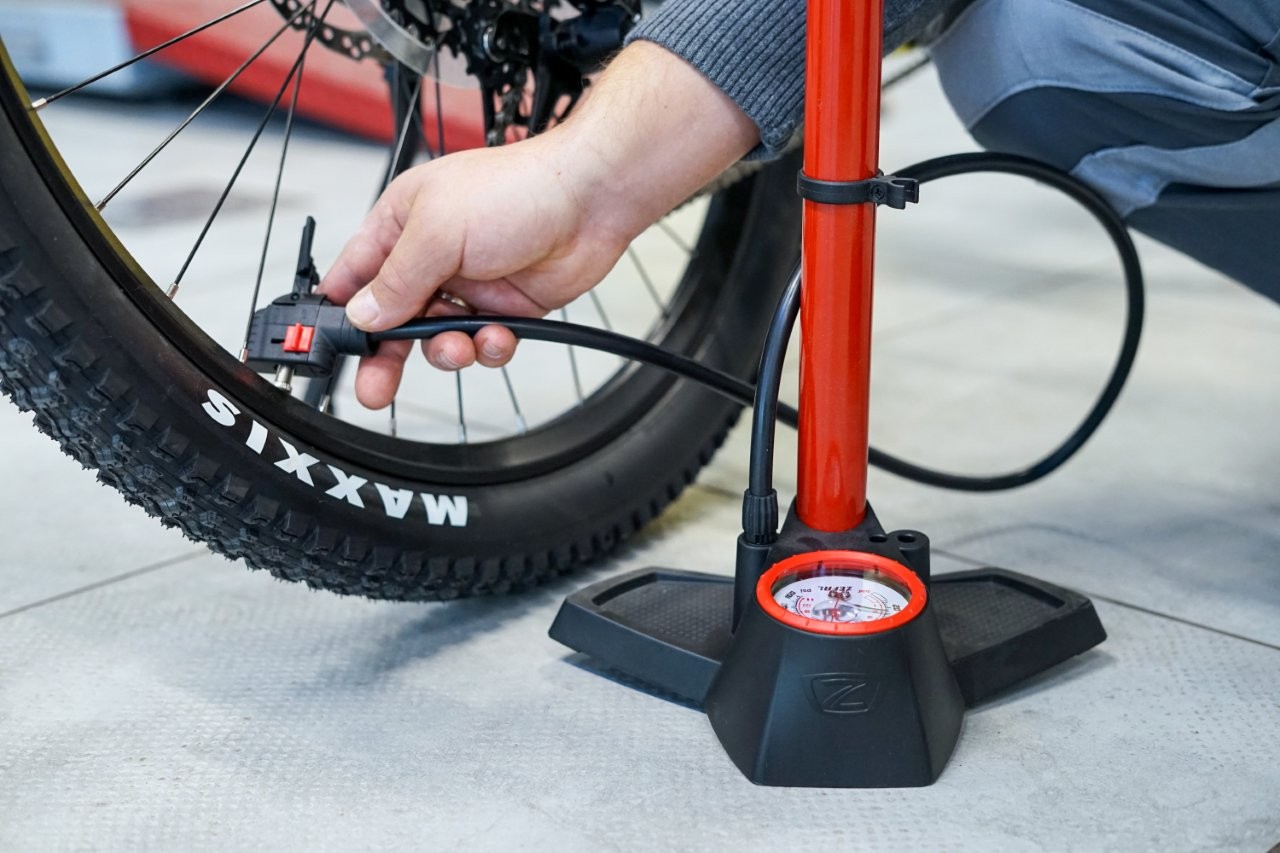 Auf dem Bild sieht man eine Hand die eine rote Fahrradpumpe an ein Rad hält