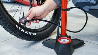 Auf dem Bild sieht man eine Hand die eine rote Fahrradpumpe an ein Rad hält