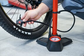 Auf dem Bild sieht man eine Hand die eine rote Fahrradpumpe an ein Rad hält