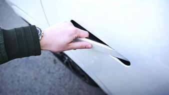 Eine Person greift zum Türgriff eines weißen Autos.