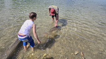 Ein Bub und ein Mann mit roter Kappe setzen einen Fisch in den See.