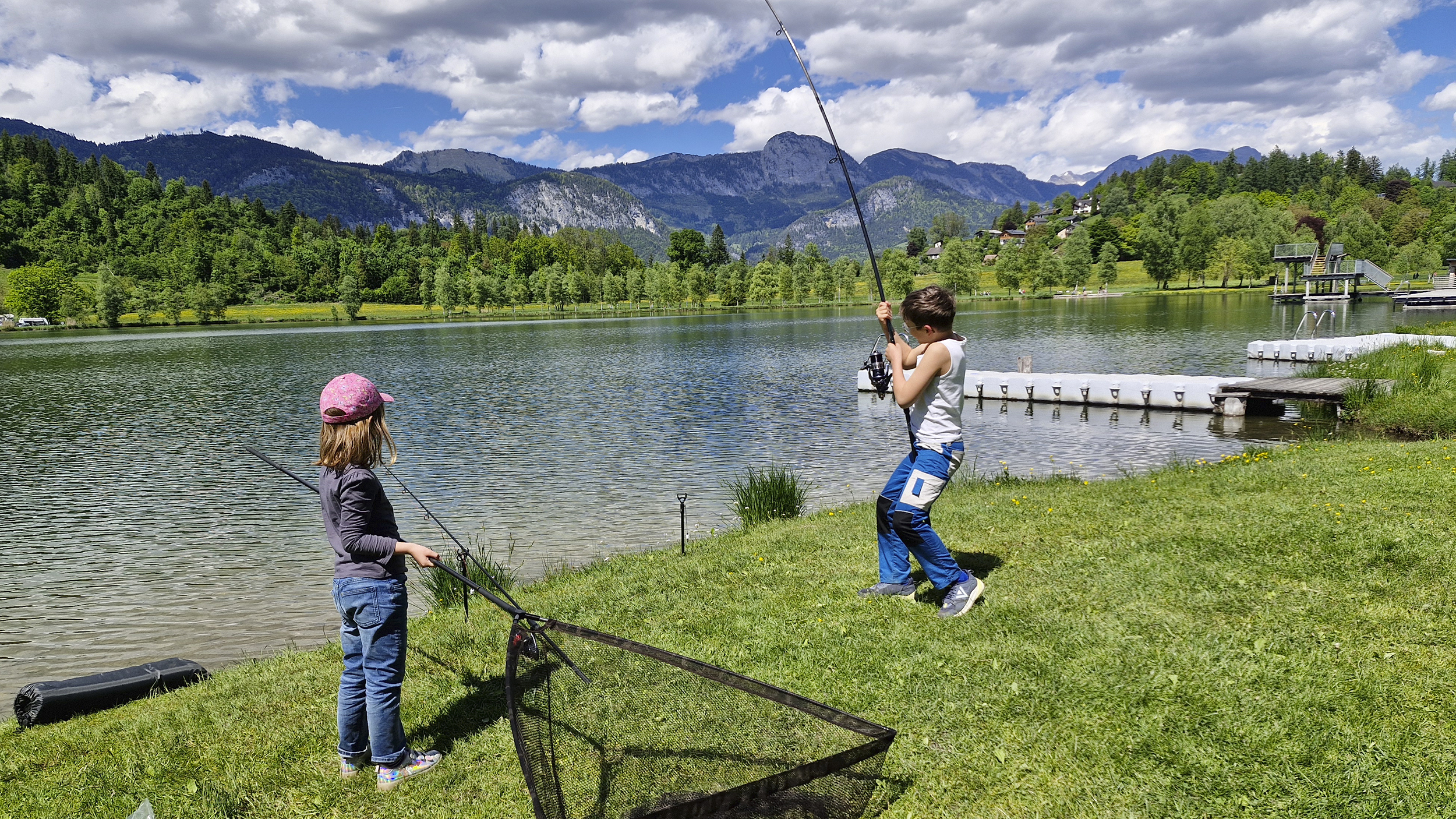 Ein Bub angelt am Putterersee, ein Mädchen steht mit einem Kescher daneben.