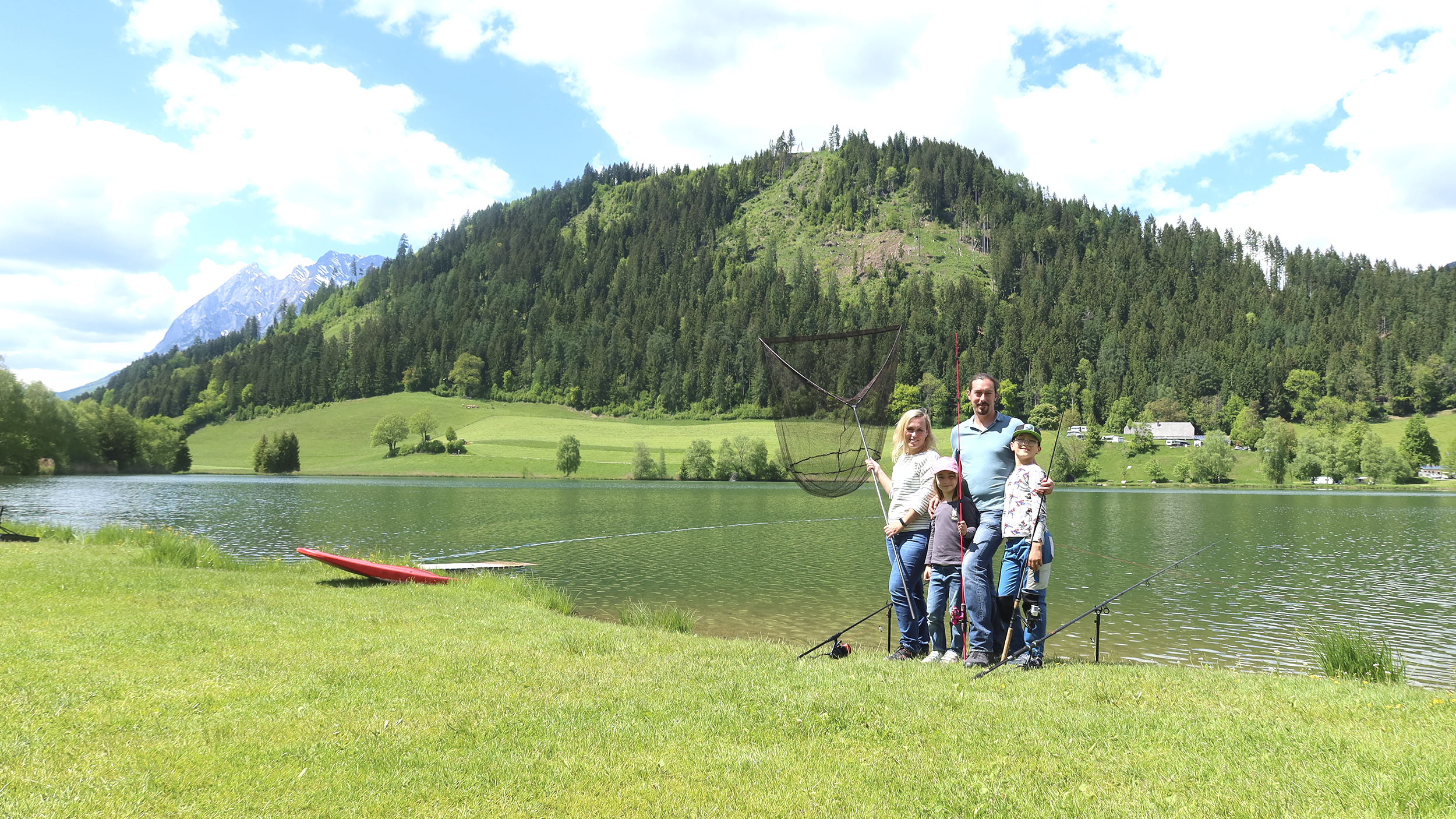 Eine Familie steht mit Angeln und Kescher am Seeufer des Putterersees.