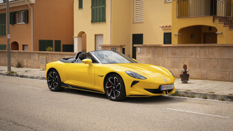 Ein gelber MG Cyberster steht auf einem Parkplatz vor einem orangenen Haus.