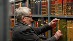 Auf dem Bild sieht man einen Mann mit Brille, der ein altes Buch aus einem Regal zieht.