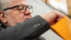 Auf dem Bild sieht man die Nahaufnahme eines Gesichts eines Mannes der konzentriert etwas aus einem gelben Kuvert nimmt.