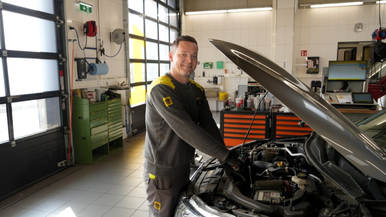 Auf dem Bild sieht man einen Mitarbeiter des ÖAMTC vor einem Auto dessen Motorhaube geöffnet ist