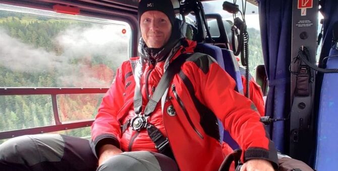 Auf dem Bild sieht man einen Bergretter in rotem Gewand, der in einem Hubschrauber sitzt.