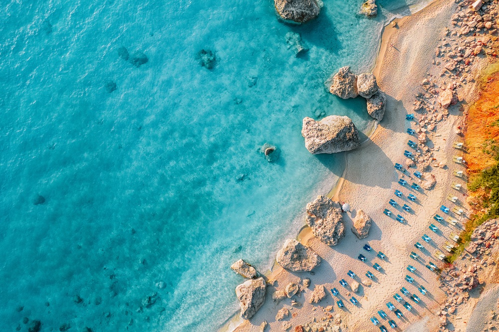 Das Bild ist eine Fotoaufnahme von oben, es ist Meer und Strand zu sehen.