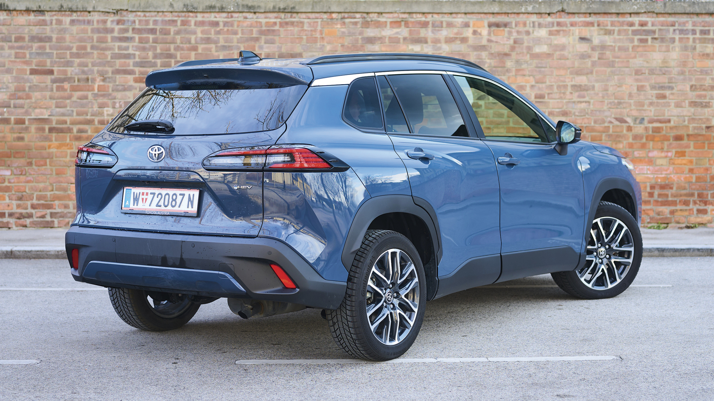 Ein graublaues Toyota-SUV steht vor einer Ziegelwand, von schräg hinten.