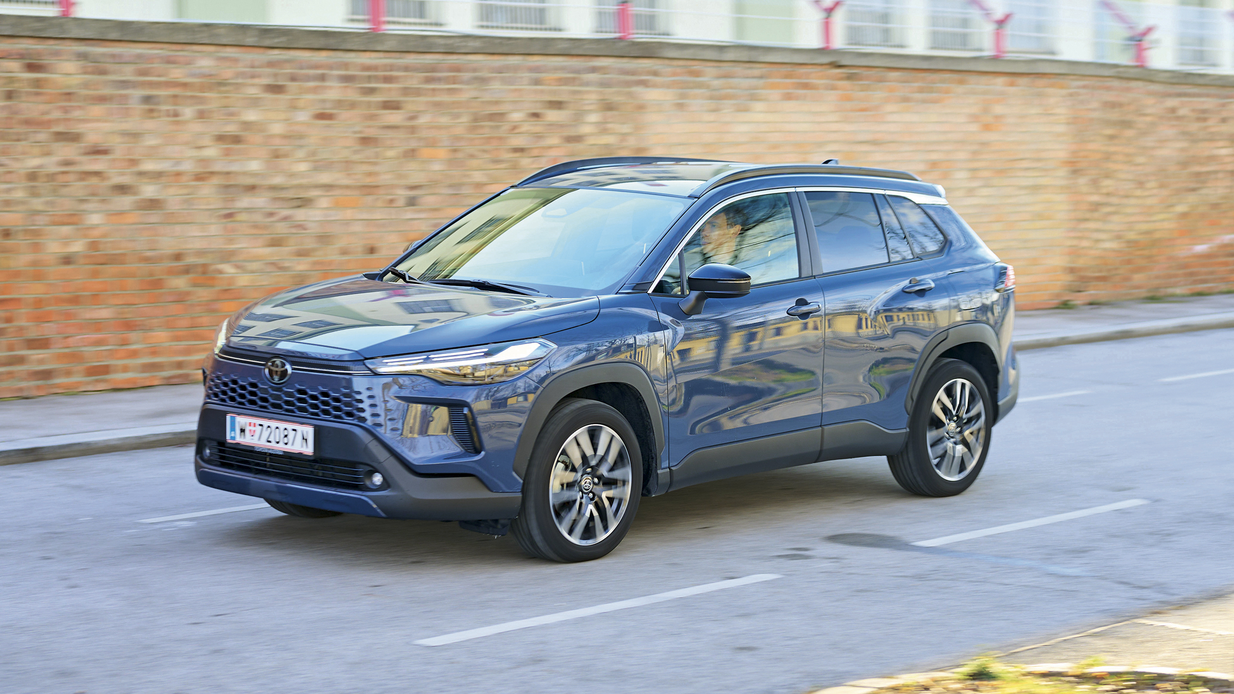 Ein graublaues Toyota-SUV fährt an einer Ziegelwand vorbei.
