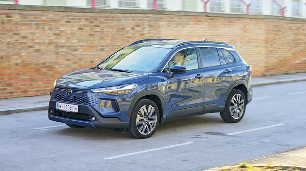 Ein graublaues Toyota-SUV fährt an einer Ziegelwand vorbei.