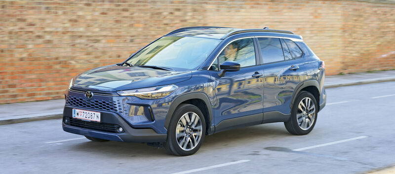 Ein graublaues Toyota-SUV fährt an einer Ziegelwand vorbei.