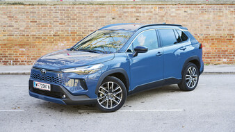 Ein graublaues Toyota-SUV steht vor einer Ziegelwand, von schräg vorne.