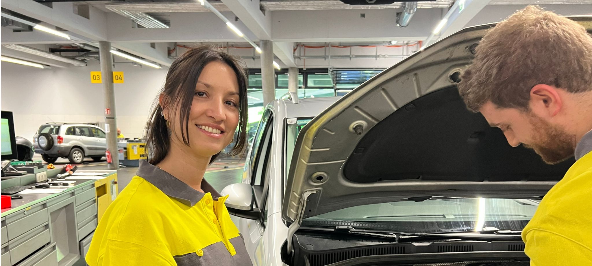 Das Bild zeigt eine Frau mit Braunen Haaren, die ein ÖAMTC-Oberteil trägt un in einer Werkstatt steht.
