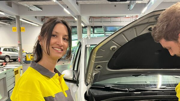 Das Bild zeigt eine Frau mit Braunen Haaren, die ein ÖAMTC-Oberteil trägt un in einer Werkstatt steht.