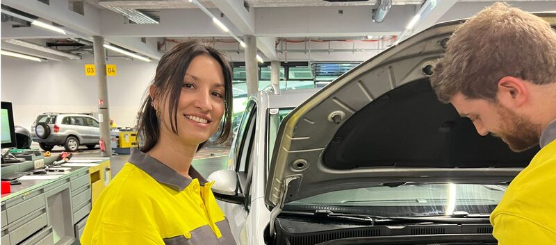 Das Bild zeigt eine Frau mit Braunen Haaren, die ein ÖAMTC-Oberteil trägt un in einer Werkstatt steht.