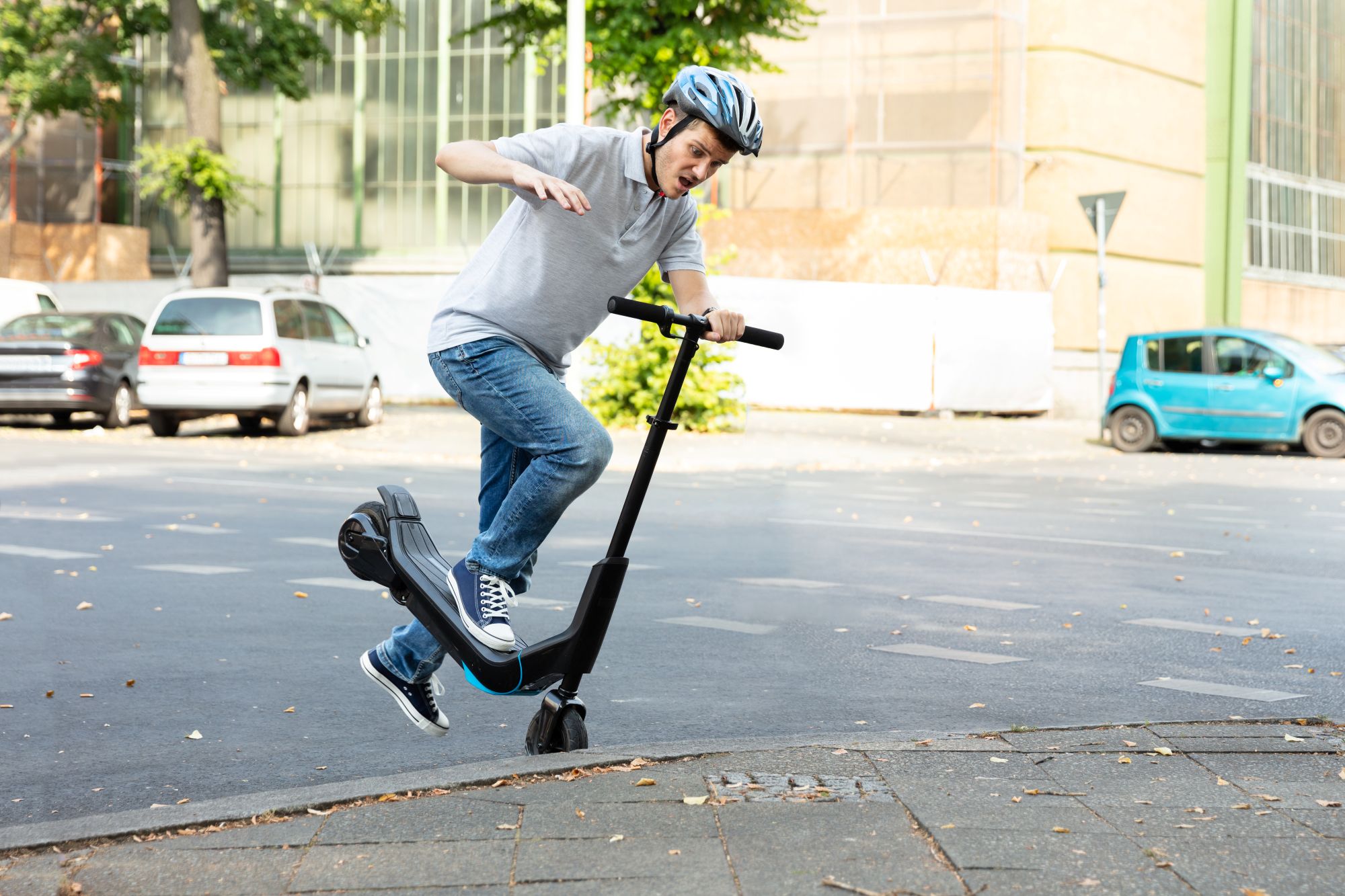Männlicher E-Scooter-Fahrer mit Helm stürzt über Bordsteinkante