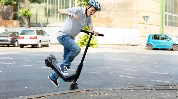 Männlicher E-Scooter-Fahrer mit Helm stürzt über Bordsteinkante