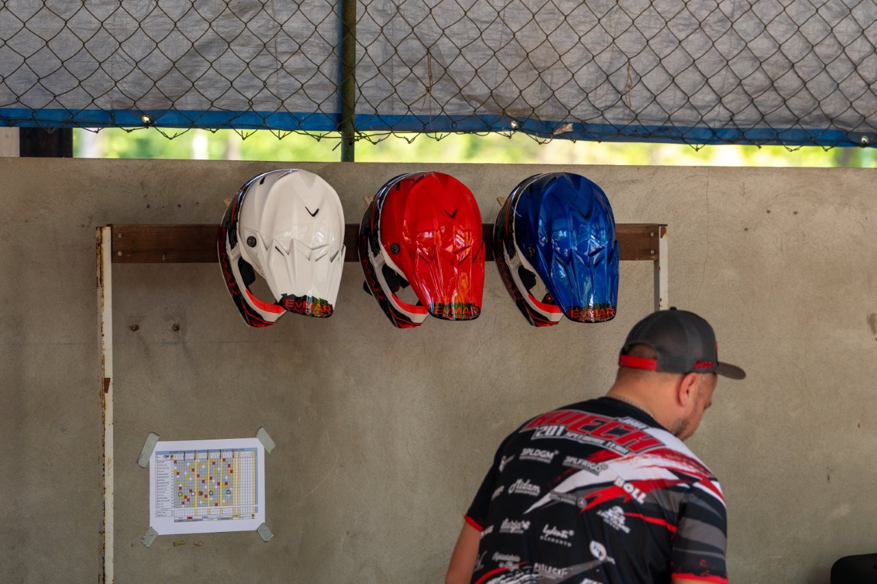 Auf dem Bild sieht man einen Mann von Hinten vor einer Mauer. An der mauer hängen ein weißer, ein roter und ein blauer Motorradhelm.