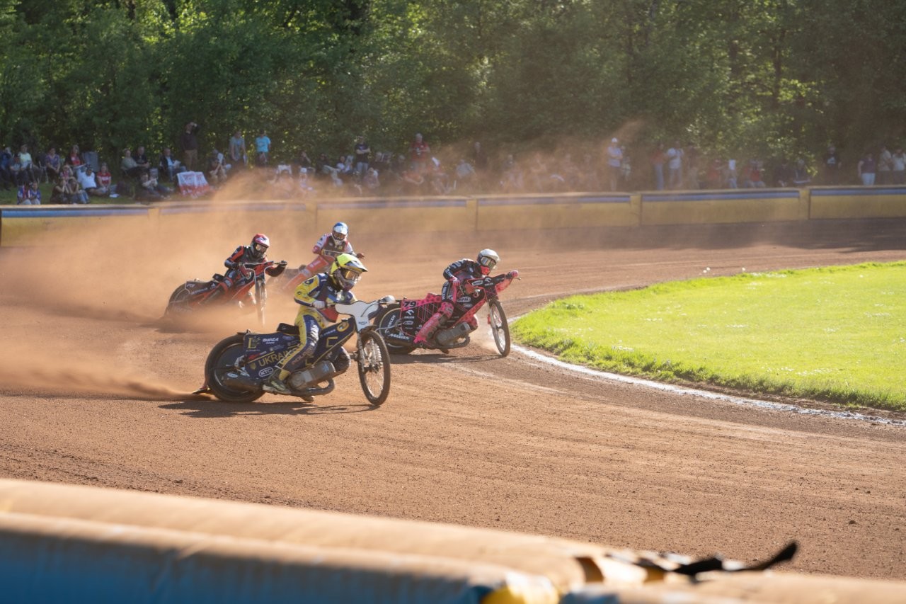 Auf dem Bild sieht man drei Speedwayfahrer in nSchräglage.