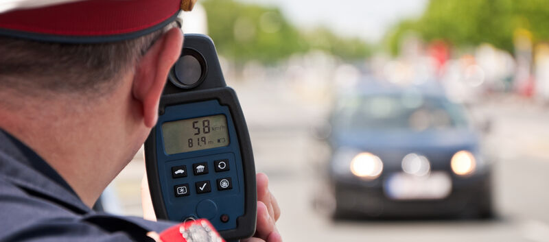 Ein Polizist misst mit einer Laserpistole die Geschwindigkeit eines schwarzen Autos.