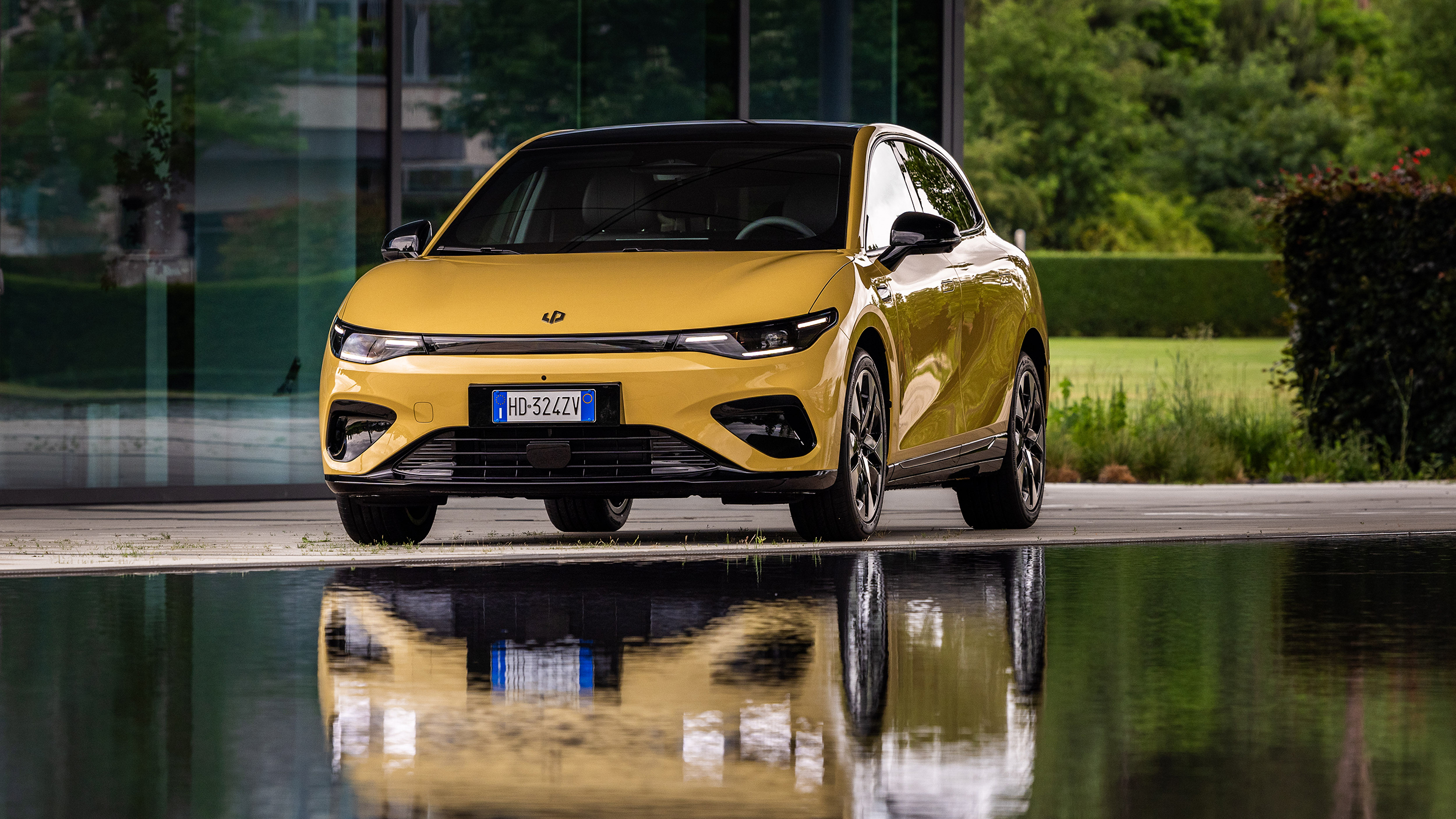 Ein gelbes Auto von vorne, das sich in einem Pool spiegelt.