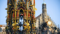 Ein bunter Brunnen im gotischen Stil, im Hintergrund eine Kirche.