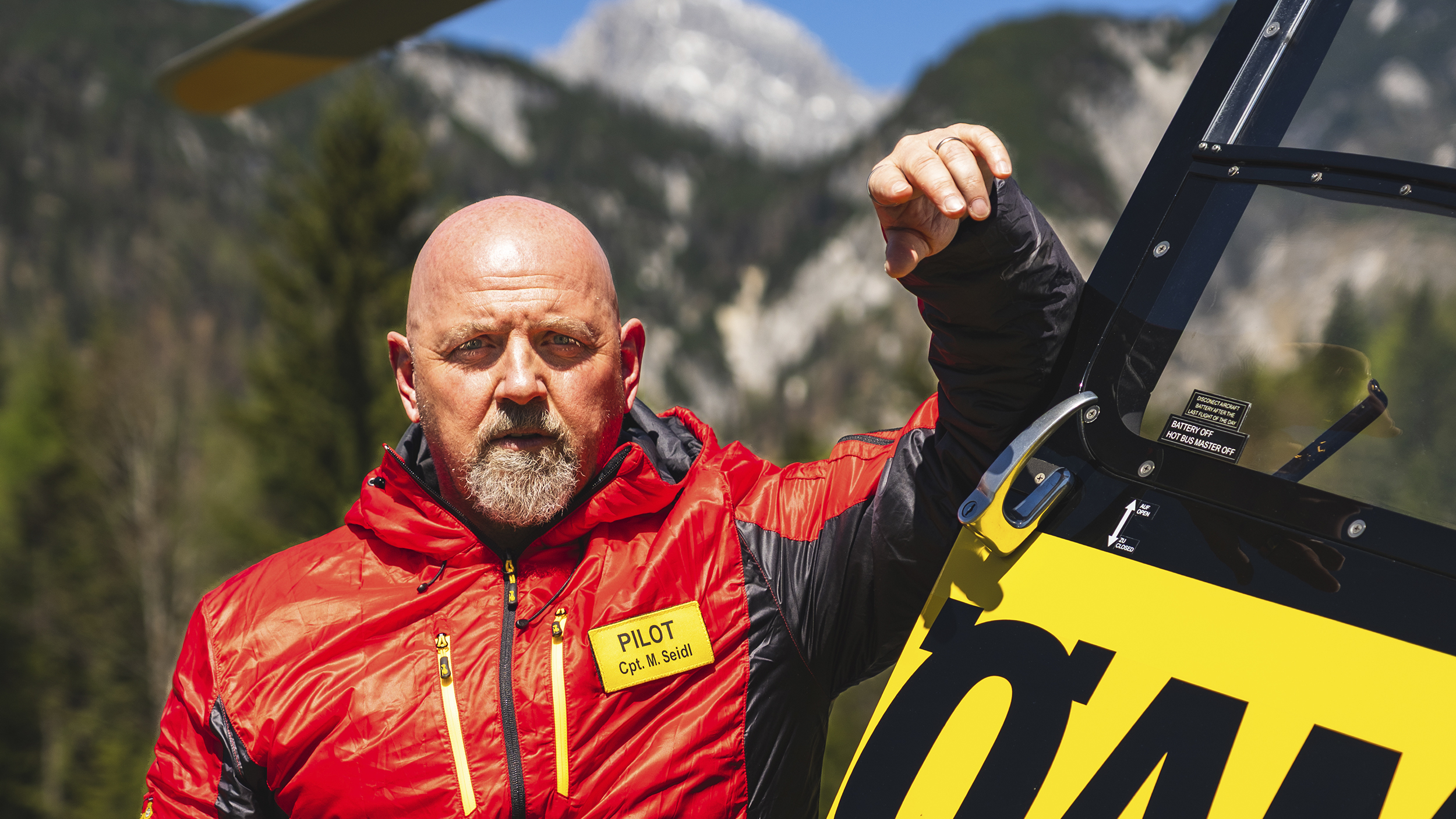 Christophorus Pilot Markus Seidl lehnt am Hubschrauber, im Hintergrund Berge.