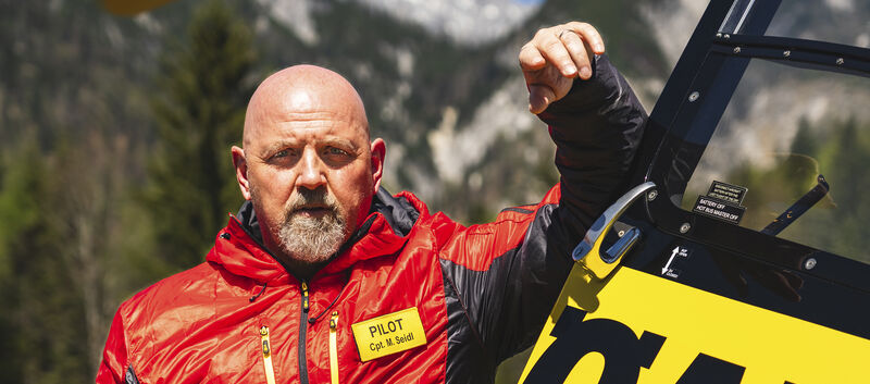 Christophorus Pilot Markus Seidl lehnt am Hubschrauber, im Hintergrund Berge.