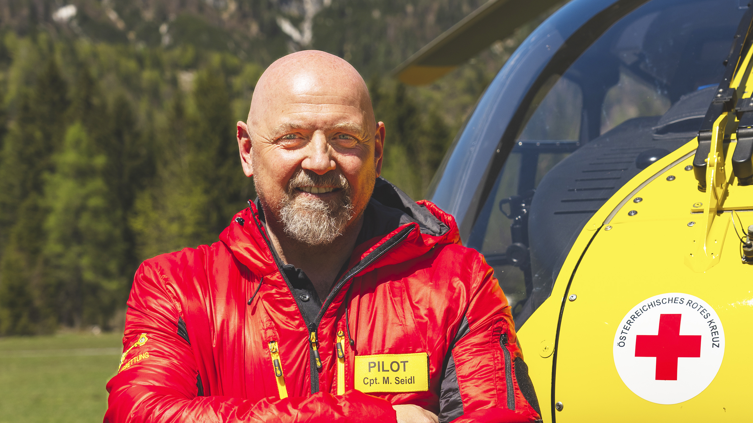 Christophorus Pilot Markus Seidl lehnt am Hubschrauber, im Hintergrund Wald.