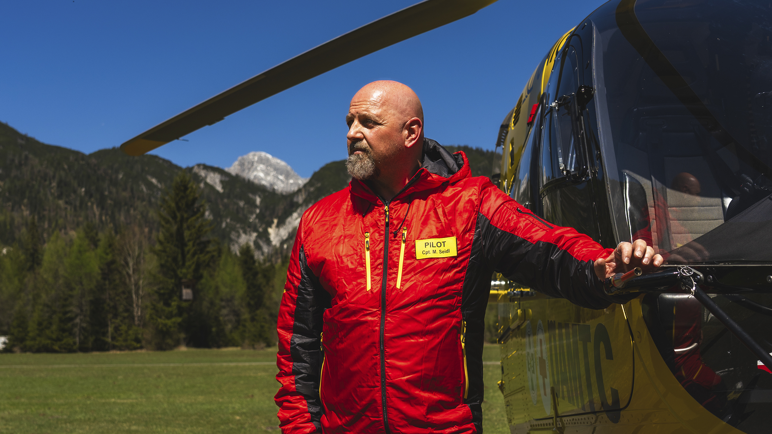 Christophorus Pilot Markus Seidl lehnt am Hubschrauber, im Hintergrund Berge.