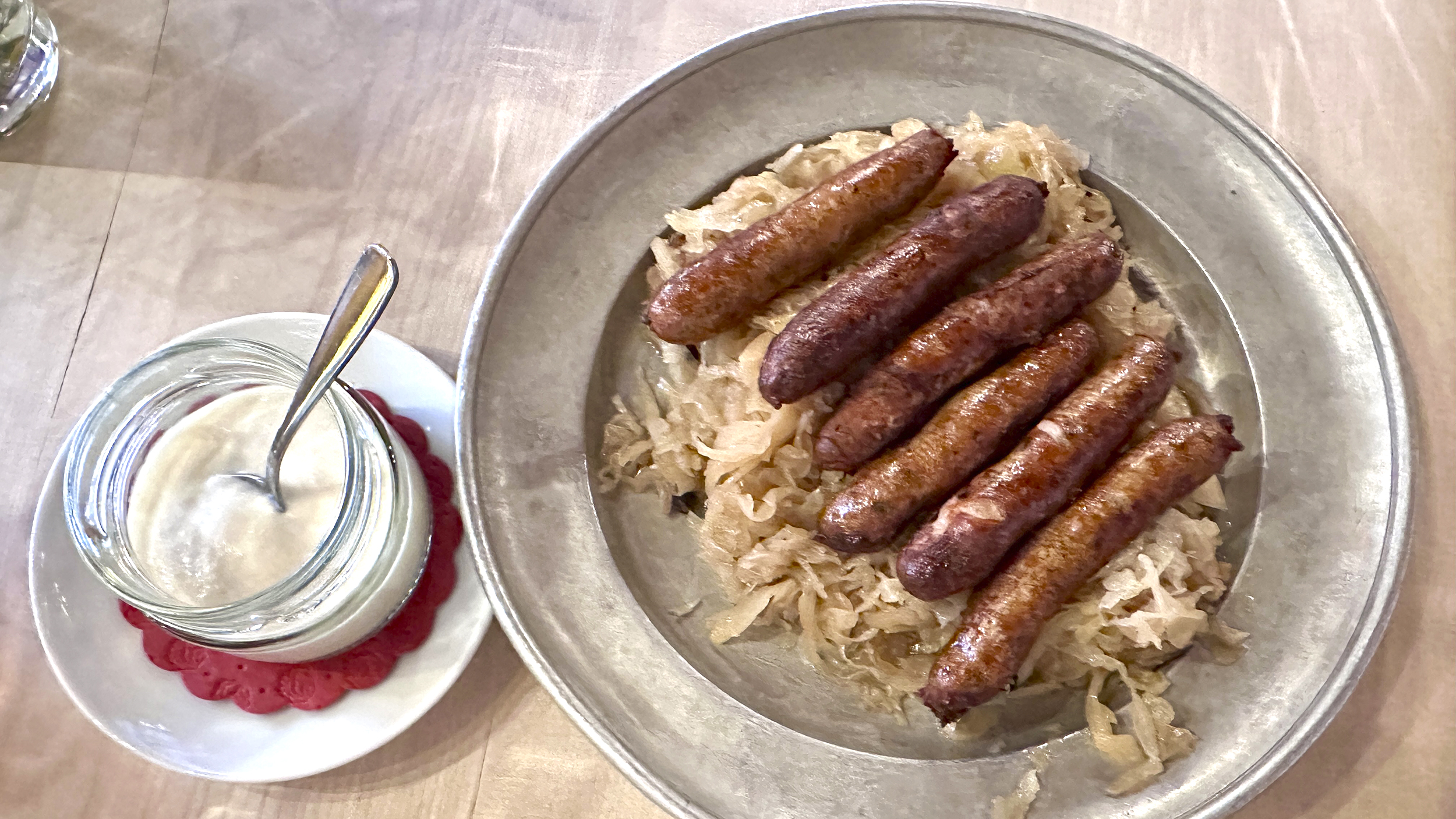 Sechs Bratwürste Auf einem Teller voll Sauerkraut, daneben eine kleine Schüssel mit Oberskren.
