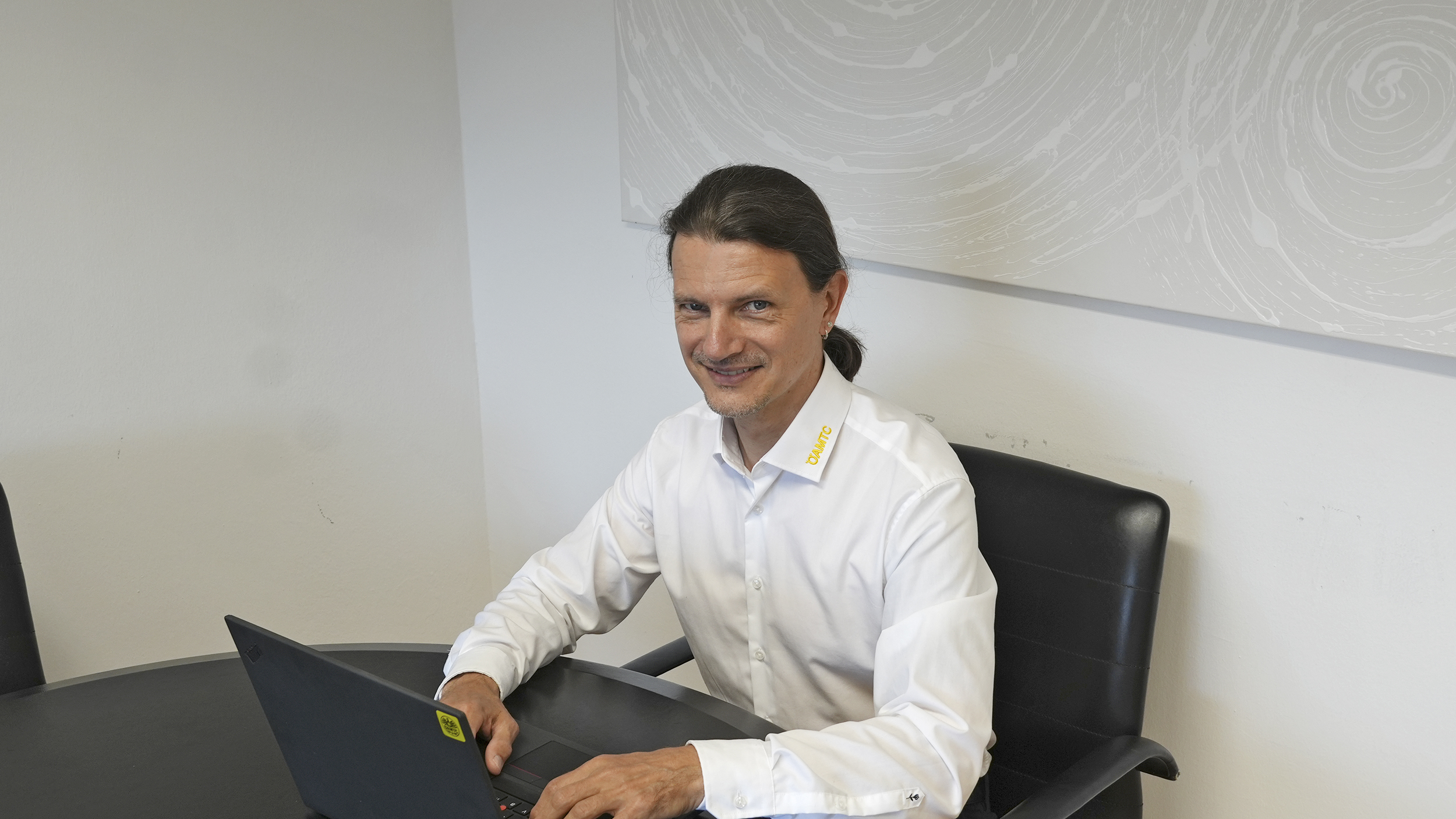 Ein Mann im weißen Hemd sitzt am Schreibtisch vor seinem Computer. Es handelt sich um Martin Eder.