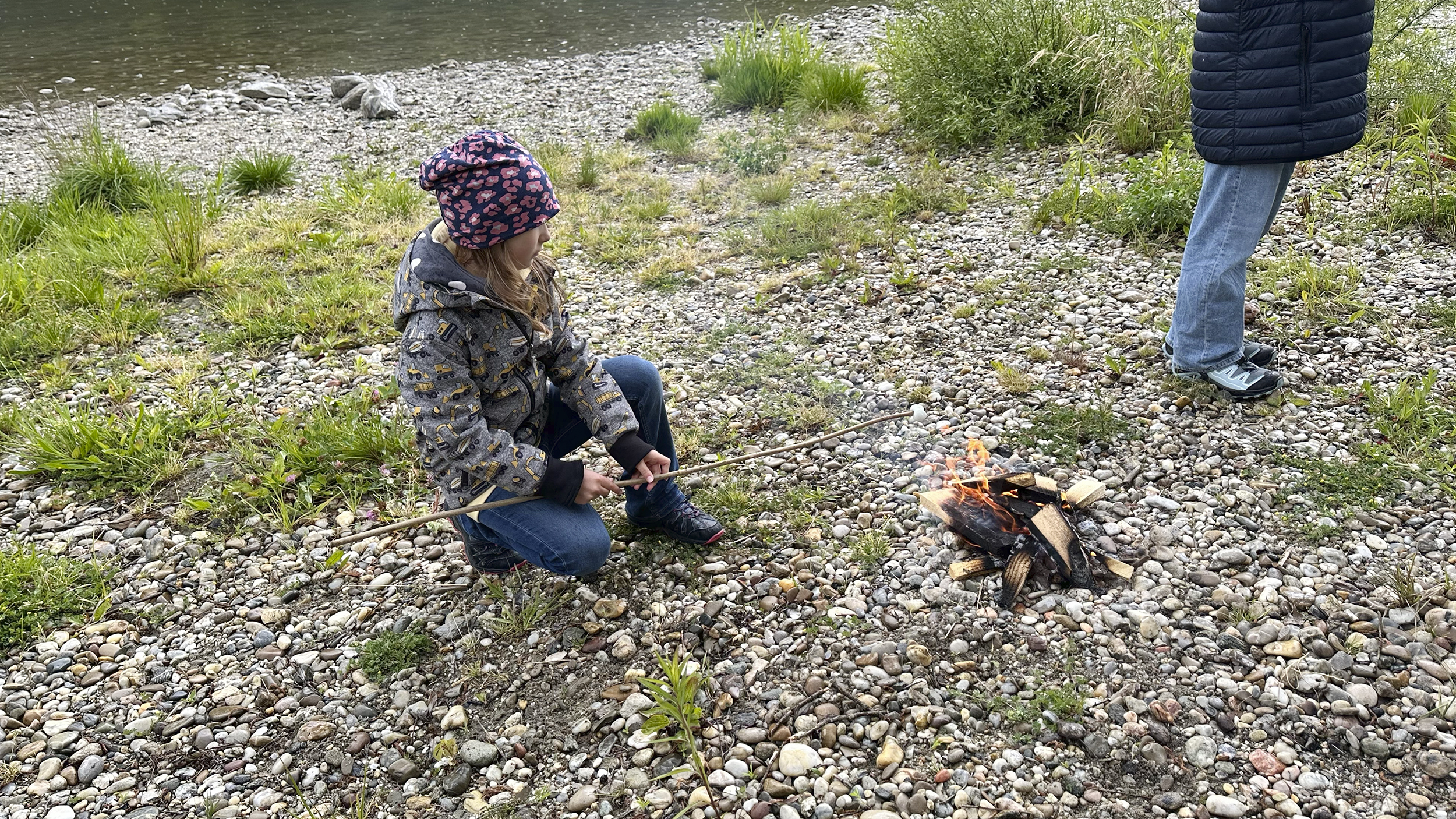 Ein Mädchen grillt Marshmallows am offenen Feuer am Donauufer.