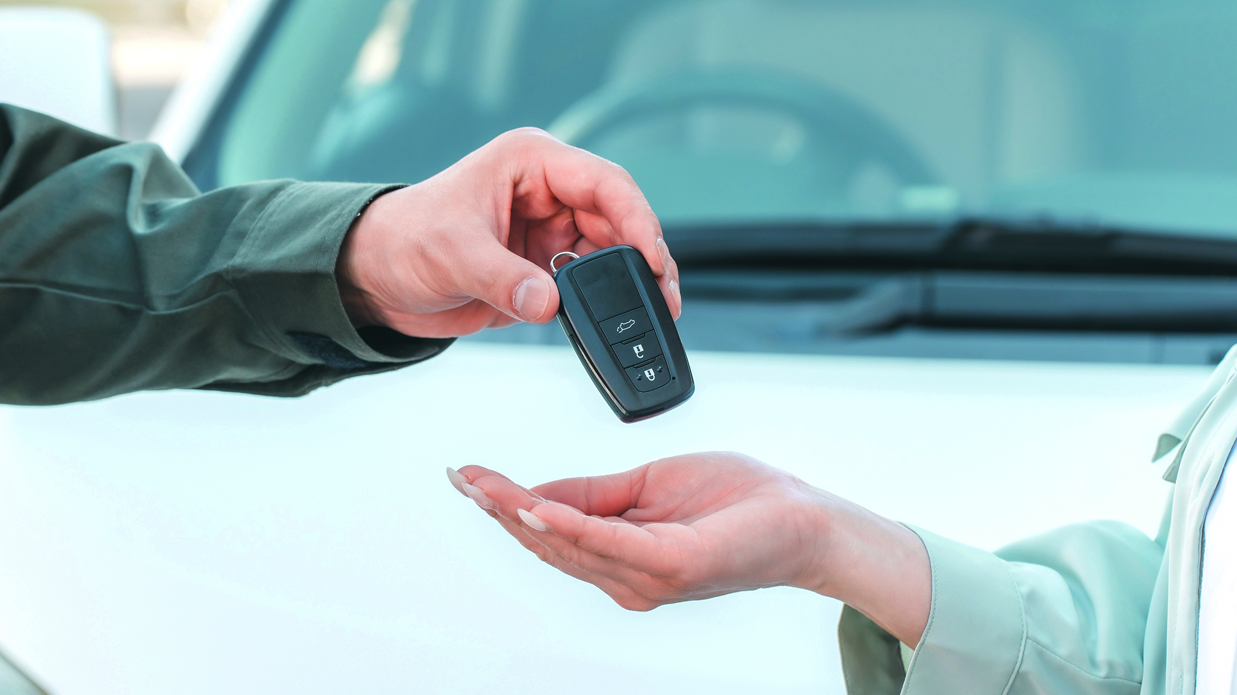 Ein Autoschlüssel wird von einer Hand in eine andere übergeben
