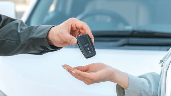 Ein Autoschlüssel wird von einer Hand in eine andere übergeben
