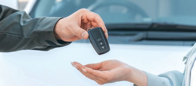 Ein Autoschlüssel wird von einer Hand in eine andere übergeben