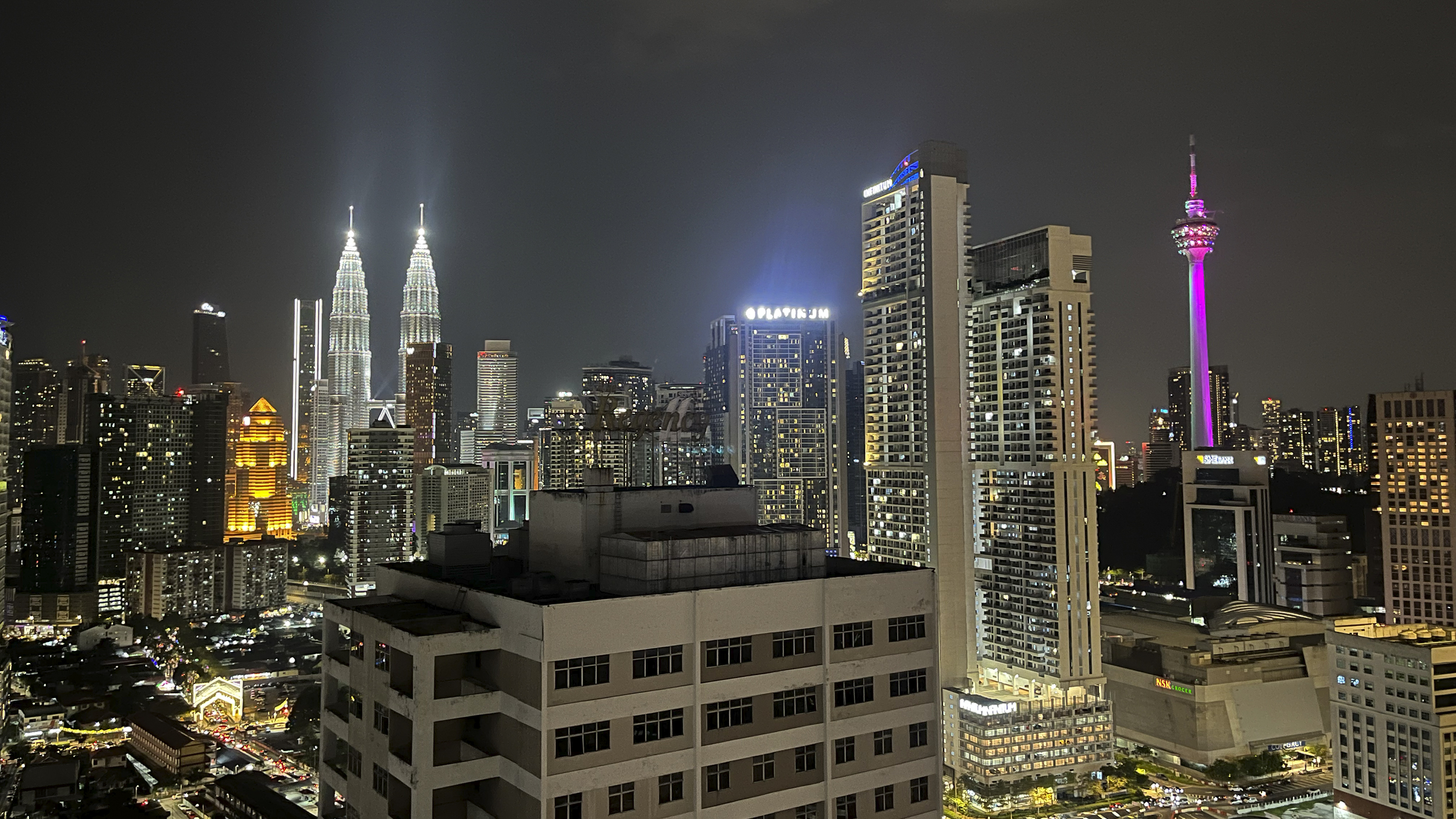Die Skyline der Stadt Kuala Lumpur in der Nacht fotografiert mit den beleuchteten Petronas Towers links im Bild.