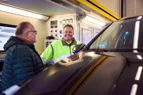 Auf dem Bild sieht man einen Techniker des ÖAMTC im Gespräch mit einem Mitglied. Im Vordergrund sieht man die Motorhaube eines Autos.