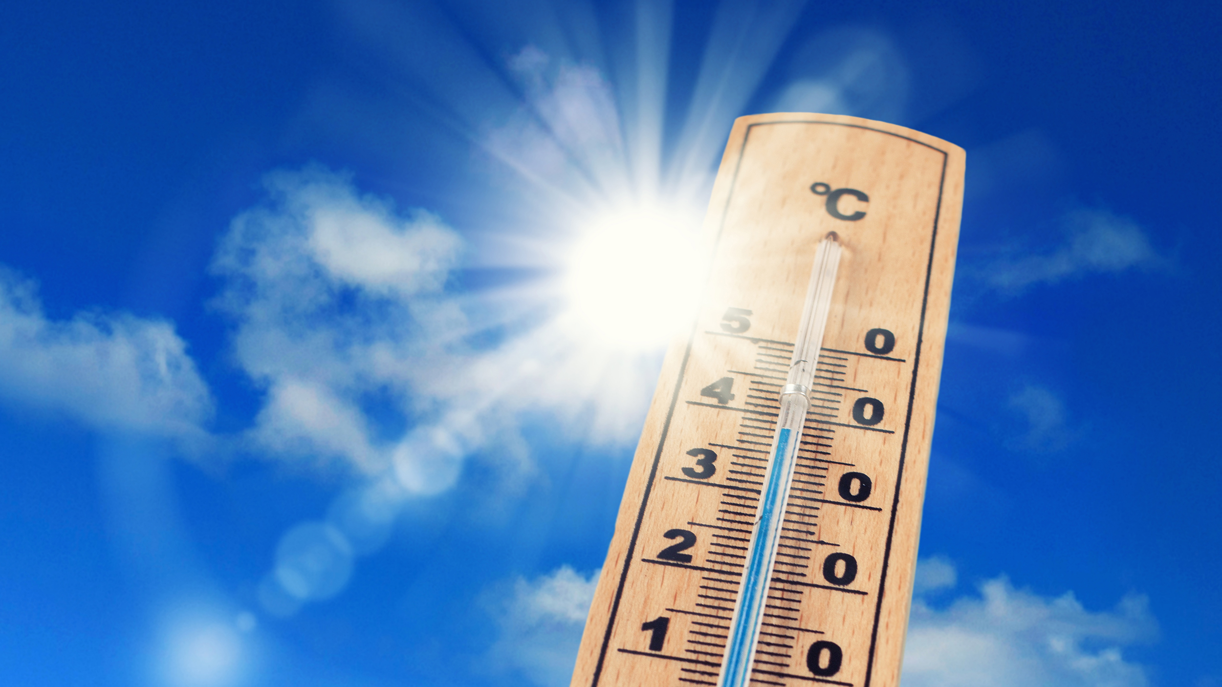 Ein altmodischer Thermometer vor blauem Himmel und strahlender Sonne.