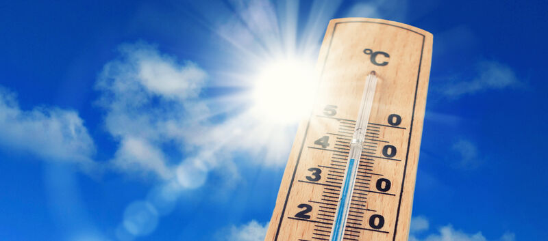 Ein altmodischer Thermometer vor blauem Himmel und strahlender Sonne.