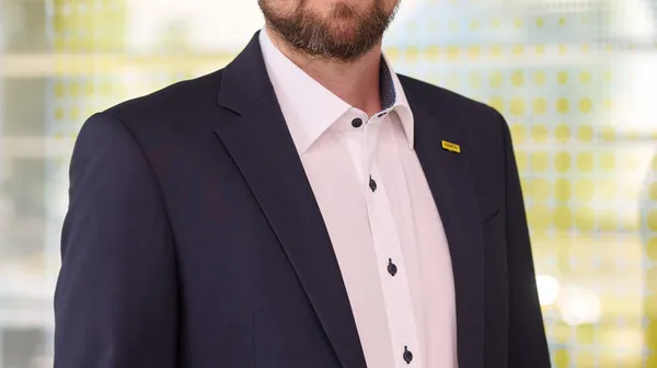Porträtfoto eines jungen Mannes mit dunklen kurzen Haaren, Bart und dunkelblauem Sakko und weißem Hemd