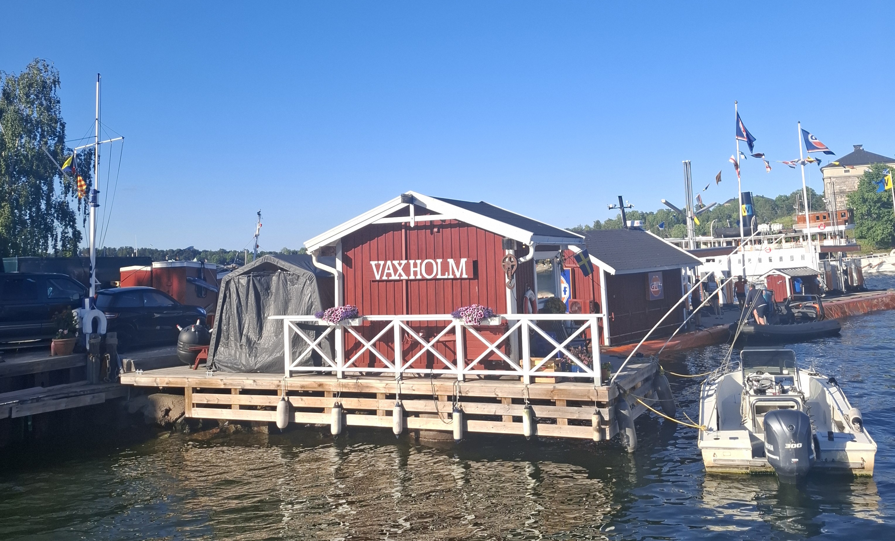 Auf dem Foto sieht man ein Rotes Bootshaus auf dem "Vaxholm" steht.
