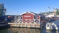 Auf dem Foto sieht man ein Rotes Bootshaus auf dem "Vaxholm" steht.