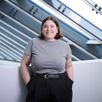 Das Bild zeigt eine Frau mit braunen Haare, die eine graues T-shirt trägt.