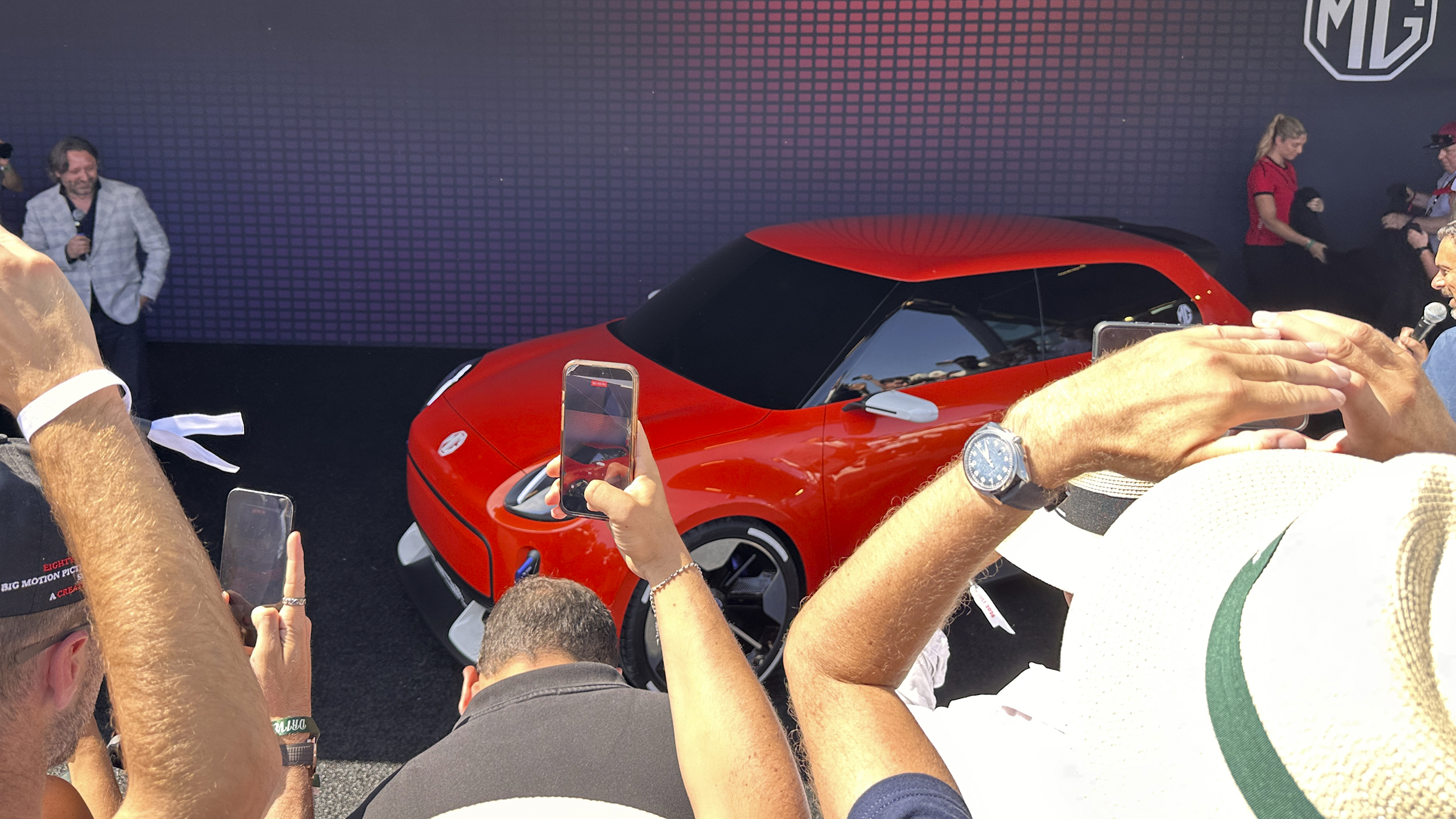 Ein orangefarbenes Auto wird von vielen Menschen mit ihren Smartphones fotografiert.