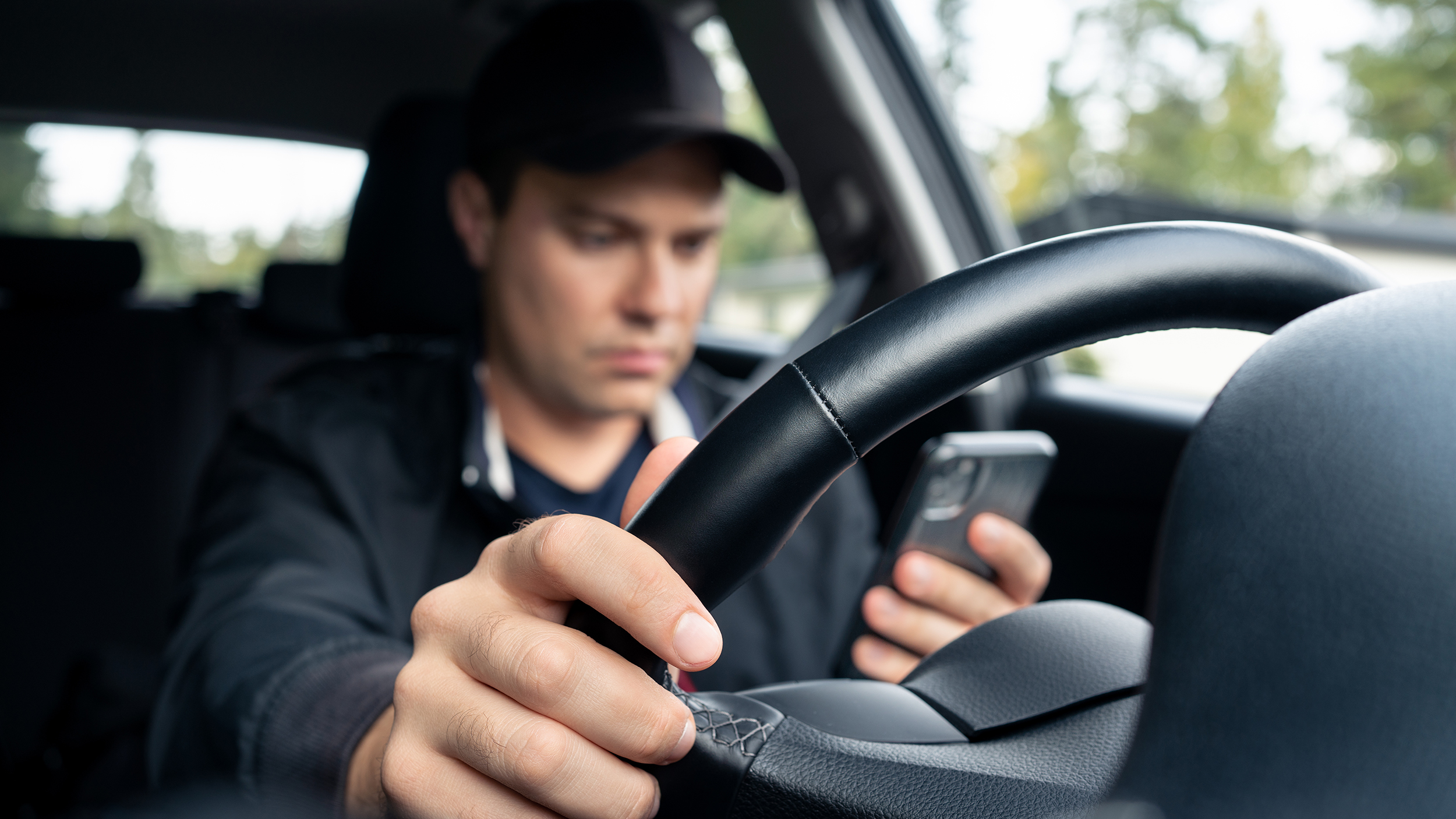 Ein Mann mit Baseballkappe nutzt sein Handy, während er Auto fährt.