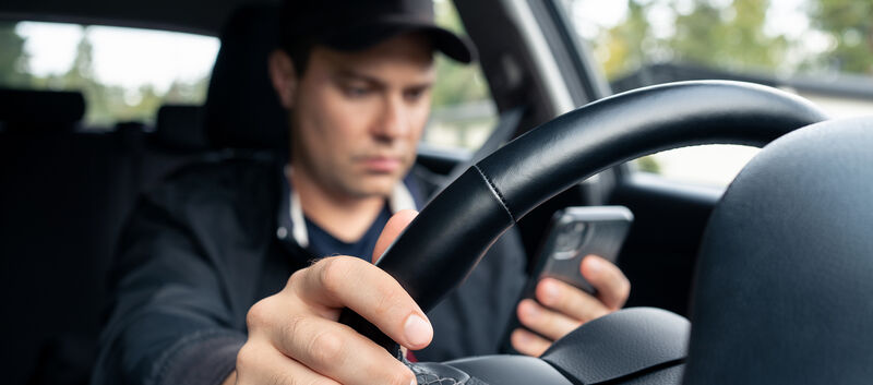 Ein Mann mit Baseballkappe nutzt sein Handy, während er Auto fährt.
