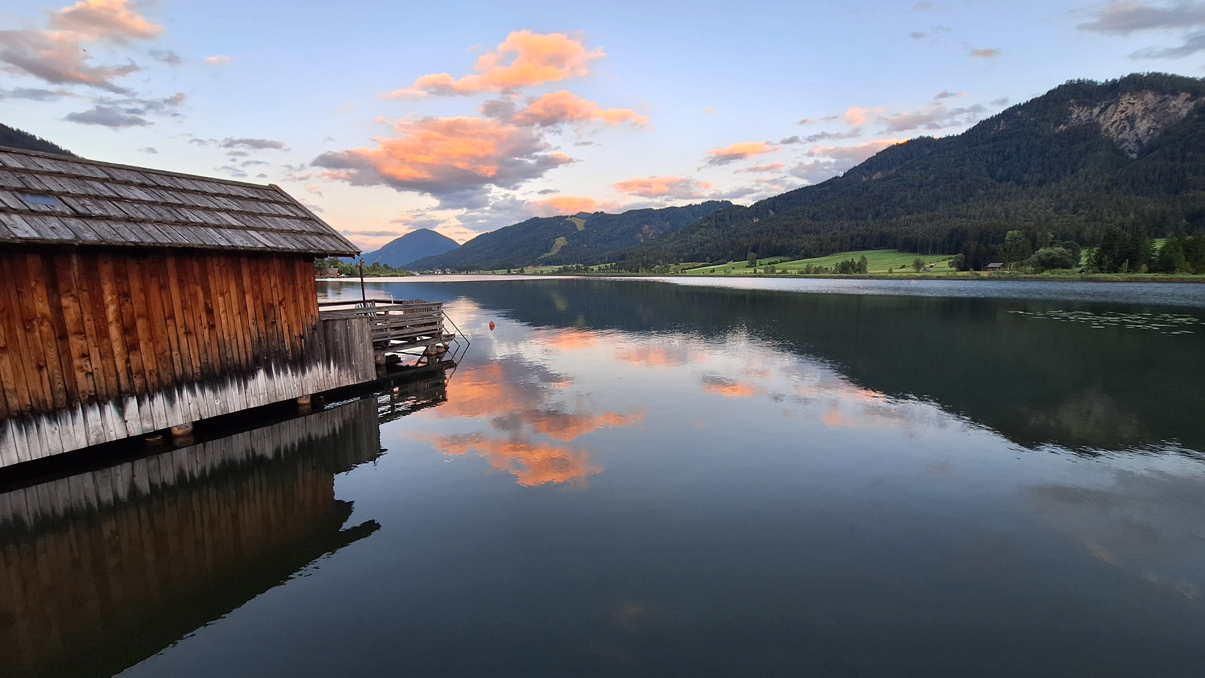 Das Foto zeigt den Weissensee, auf der linken Seite sieht man ein Holzhaus und recht einen Berg.